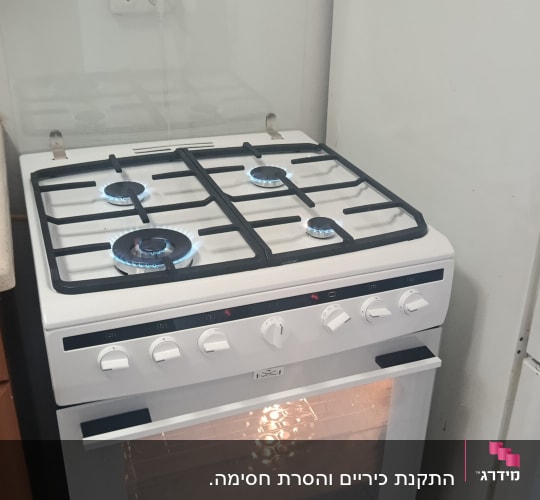 תנור גז לבן עם כיריים דולקות במטבח